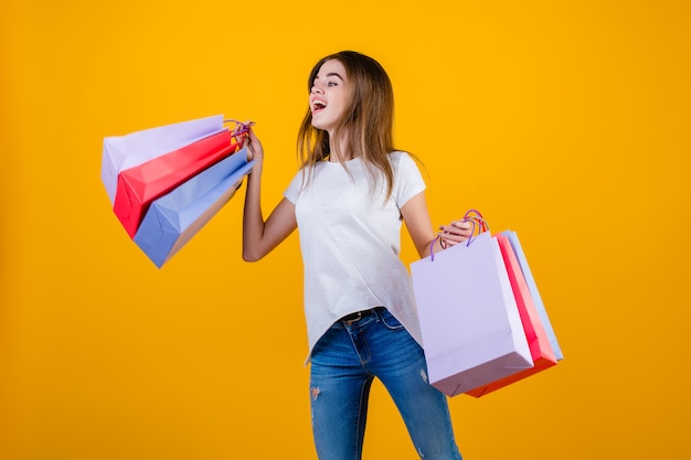 Feliz sonriente mujer morena hermosa con coloridas bolsas de papel saltando en el aire aislado sobre amarillo