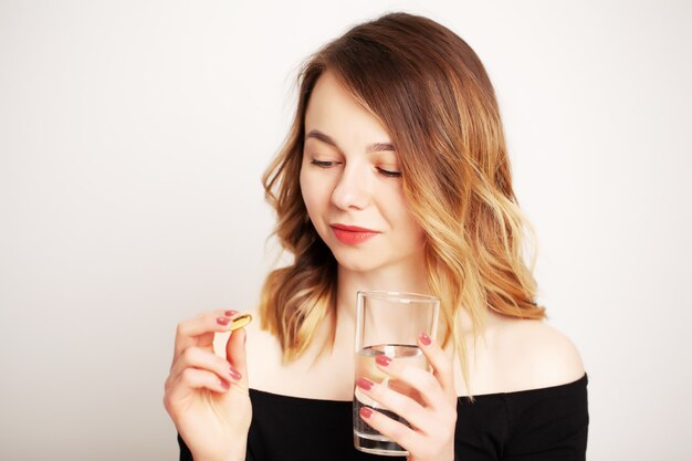 Feliz sonriente mujer positiva comiendo la píldora y sosteniendo el vaso de agua en la mano, en su casa