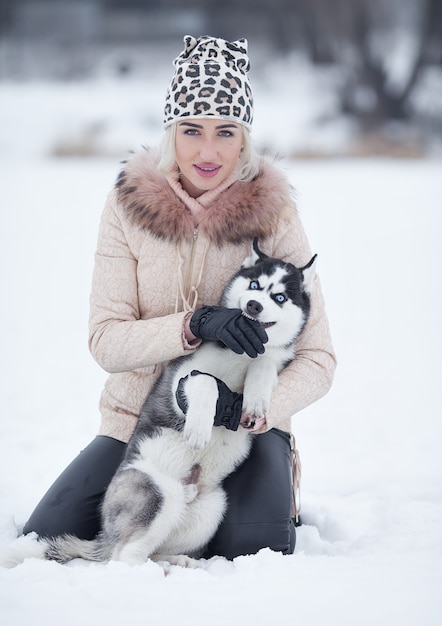 Feliz sonriente mujer rubia caucásica y su perro Husky. Jugando al aire libre en invierno bosque blanco juntos.