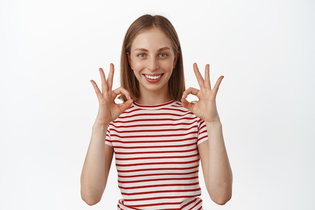 Feliz sonriente mujer rubia da su garantía, mostrando ok, ok, cero gestos y asentir en aprobación, asegurar todo bajo control, elogiar el excelente resultado, recomendar algo.