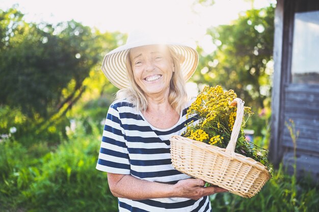 Feliz sonriente mujer senior posando en el jardín de verano con flores.