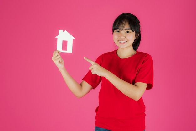 Foto feliz sonriente niña asiática de pie con casa de papel sobre fondo rosa