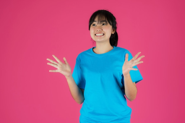 Feliz sonriente niña asiática de pie con expresión facial sorpresa sobre fondo rosa