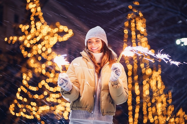 Feliz sonriente niña caucásica quema bengalas por iluminación navideña en la víspera de año nuevo