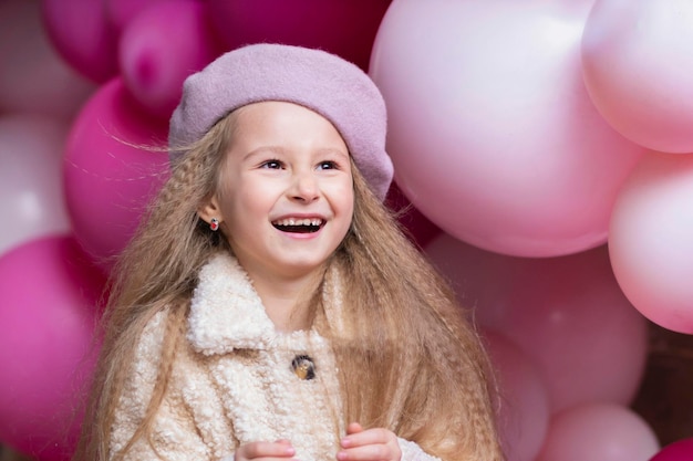 Feliz sonriente niña emocional en boina jugando con globos de color rosa, púrpuras. Concepto de fiesta de cumpleaños para niños