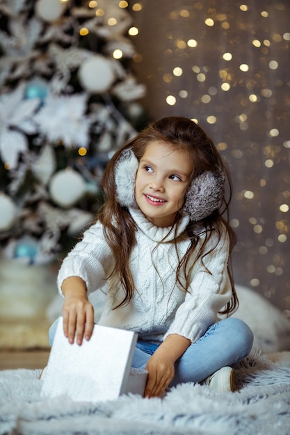 Feliz sonriente niña niño abriendo caja de regalo cerca del árbol de Navidad decorado con luces