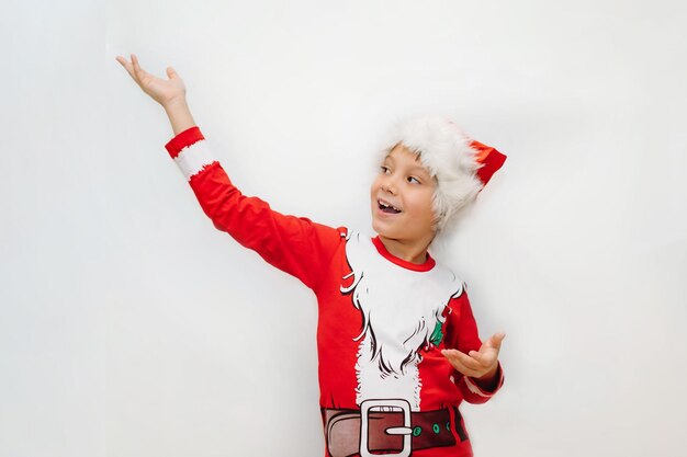 Feliz sonriente niño caucásico en santa camiseta y sombrero apuntando al espacio en blanco sobre fondo blanco para texto publicitario. Foto de alta calidad