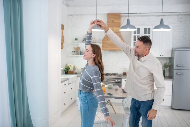 Feliz sonriente padre e hija cogidos de la mano bailando en casa.