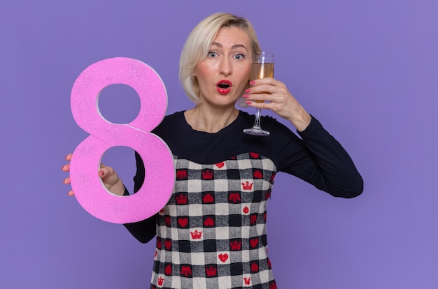 Feliz y sorprendida joven sosteniendo el número ocho y una copa de champán celebrando la marcha del día internacional de la mujer