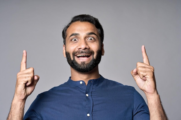 Feliz sorprendido hombre de negocios indio señalando con el dedo aislado en gris