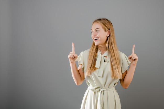 Feliz sorridente bela loira jovem apontando o dedo na copyspace isolado sobre cinza