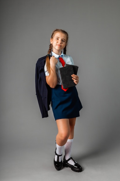 Feliz sorridente colegial de 12 anos de idade, segurando um laptop, isolado em um fundo cinza, olhando para a câmera.