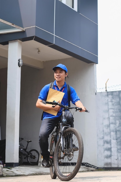 Feliz sorridente entregador de uniforme azul segurando pacote com mochila na bicicleta