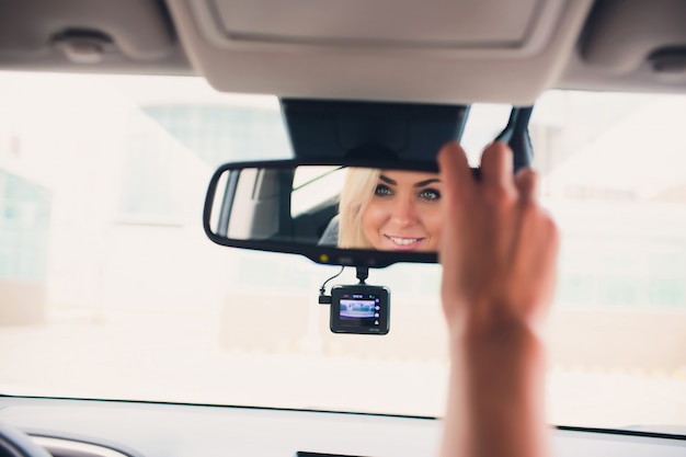 Feliz sorridente feminino regozijando-se na nova compra cara no showroom de automóveis. Cliente bonito que senta-se na porta do carro superior de dobramento branco.