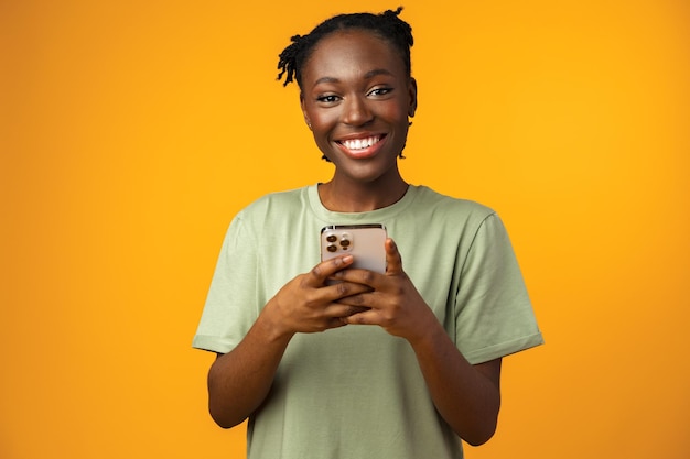 Feliz sorridente garota afro-americana usando seu smartphone no estúdio amarelo