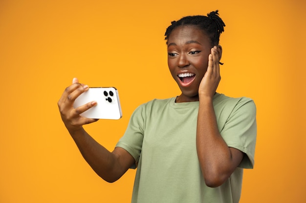 Feliz sorridente garota afro-americana usando seu smartphone no estúdio amarelo