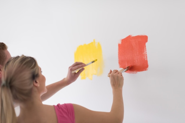 Foto feliz sorridente jovem casal pintando a parede interior da casa nova