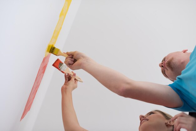 feliz sorridente jovem casal pintando a parede interior da casa nova