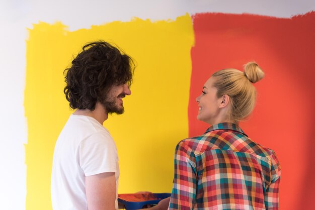 Foto feliz sorridente jovem casal pintando a parede interior da casa nova