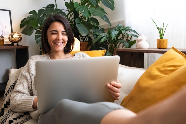 Feliz sorridente jovem caucasiana usando laptop deitado no sofá em casa aconchegante sala de estar Copiar espaço Estilo de vida e conceito de tecnologia