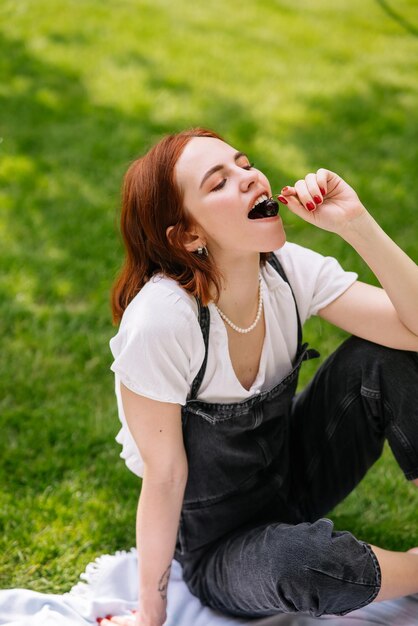 Feliz sorridente jovem comendo cereja do gramado do parque