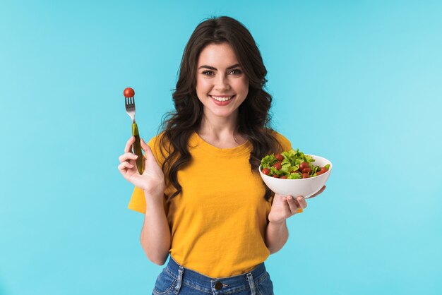 Foto feliz sorridente jovem isolada sobre a parede azul segurando salada.