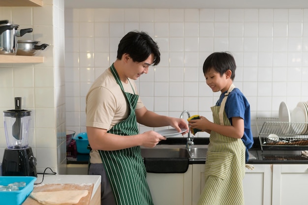 Feliz sorridente jovem pai asiático e filho lavando pratos na cozinha em casa