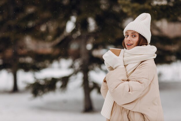 Feliz sorridente jovem retrato de mulher vestida casaco lenço chapéu e luvas gosta do tempo de inverno no parque de inverno coberto de neve