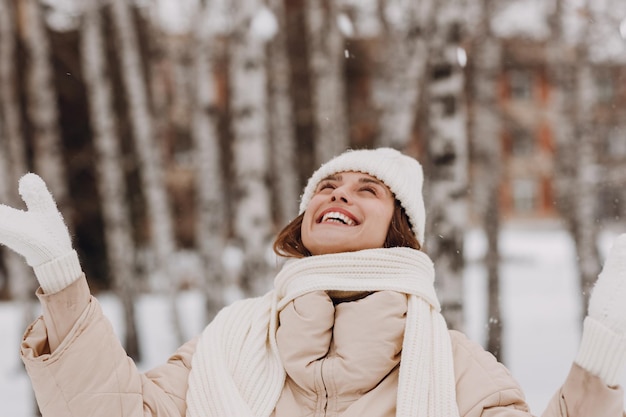 Feliz sorridente jovem retrato de mulher vestida casaco lenço chapéu e luvas gosta do tempo de inverno no parque de inverno coberto de neve