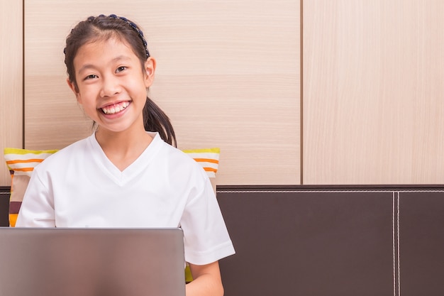 Feliz sorridente menina asiática usando computador notebook para estudar na cama dela