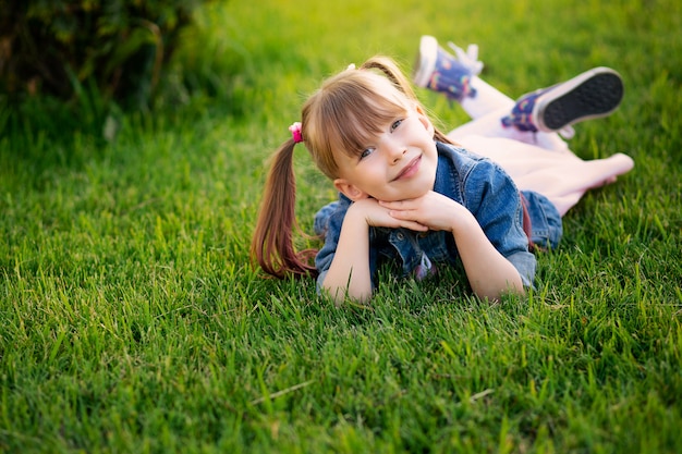 Feliz sorridente menina de seis anos encontra-se na grama do parque