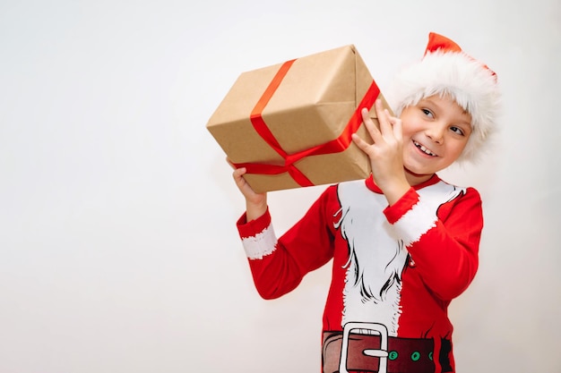 Feliz sorridente menino caucasiano em santa t-shirt e chapéu segurando uma varíola com presente de Natal. Foto de alta qualidade