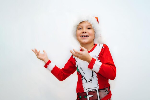 Feliz sorridente menino caucasiano na camiseta do papai noel e chapéu apontando para o espaço em branco no fundo branco para texto publicitário