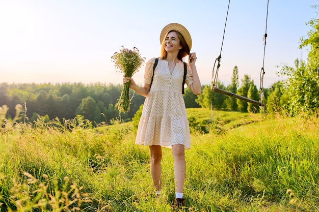 Feliz sorridente mulher adulta de vestido com chapéu com um buquê de flores silvestres