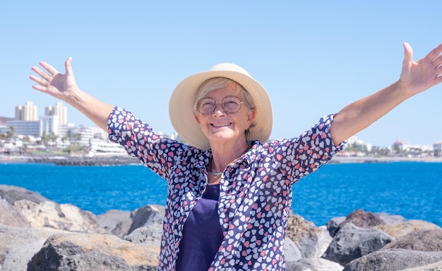 Feliz sorridente mulher caucasiana com chapéu de palha e braços estendidos desfrutando do mar e da liberdade nas férias
