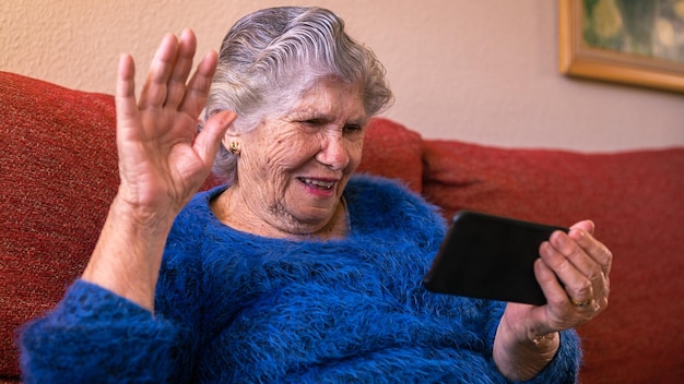 Feliz sorridente velha caída de mão em saudação enquanto estiver usando um smartphone