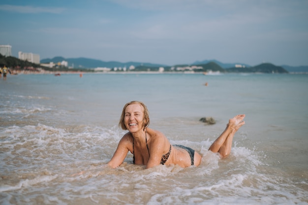 Feliz sorrindo animado turista sênior idoso jogando na água e nadar nas grandes ondas na praia do mar oceano. Viajando pela Ásia, conceito de estilo de vida ativo.