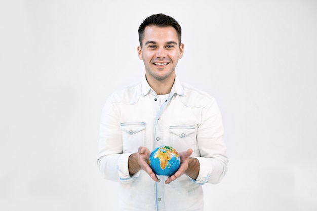 Feliz sorrindo homem caucasiano hipster em roupas casuais brancas, segurando o globo da terra contra um fundo branco isolado