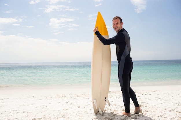 Feliz surfista sosteniendo una tabla de surf en la playa