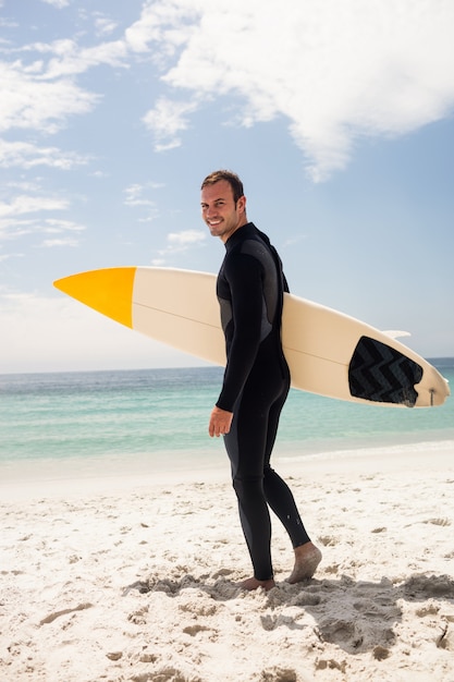 Feliz surfista sosteniendo una tabla de surf en la playa