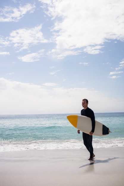 Feliz surfista sosteniendo una tabla de surf en la playa