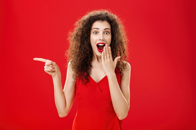 Feliz, surpresa e encantada mulher atraente de cabelos cacheados em vestido de noite, sorrindo maravilhada com ope ...