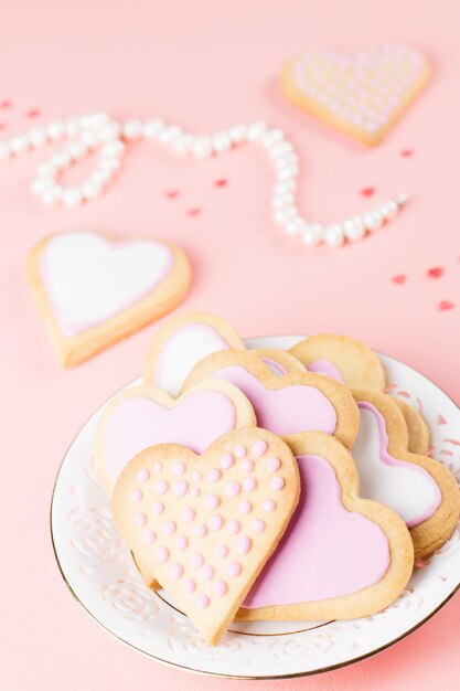 Feliz tarjeta de felicitación del día de San Valentín con galletas de corazón, copas de vino y vino sobre fondo rosa pastel.