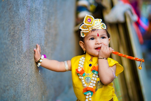 Foto feliz tarjeta de felicitación de janmashtami que muestra a un niño indio haciéndose pasar por shri krishna o kanha / kanhaiya con imagen de dahi handi y flores de colores.