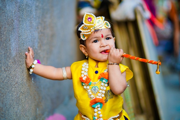 Foto feliz tarjeta de felicitación de janmashtami que muestra a un niño indio haciéndose pasar por shri krishna o kanha / kanhaiya con imagen de dahi handi y flores de colores.