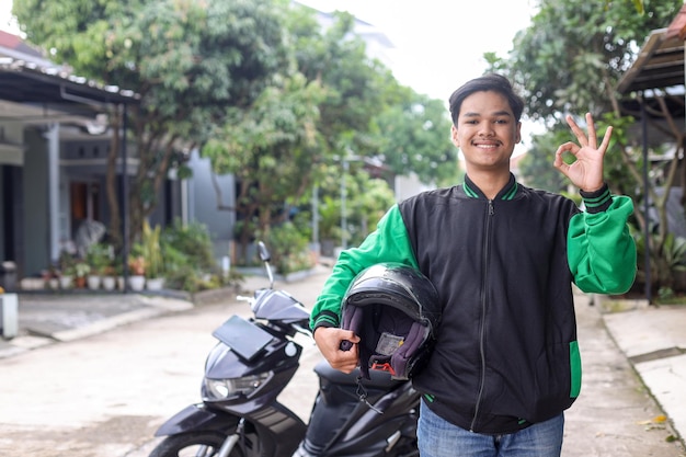 Feliz taxista de motocicleta comercial sosteniendo casco y dando un gesto de aprobación