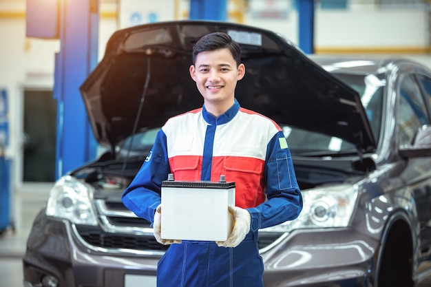 Feliz técnico o mecánico de automóviles Tranquilizar la batería del automóvil en el centro de servicio de reparación de automóviles.