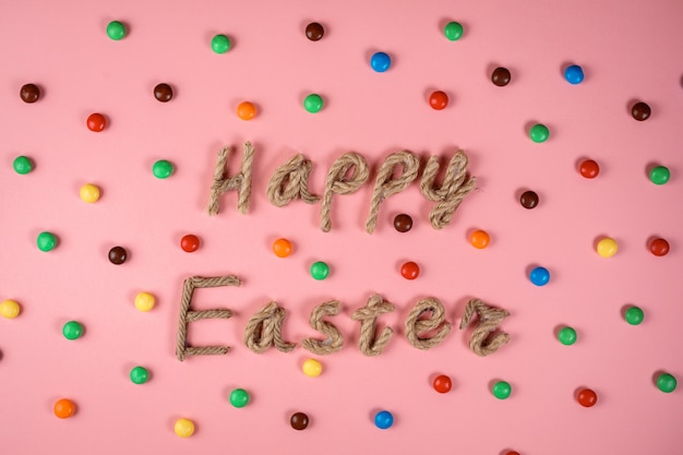 Feliz tipografía de Pascua en estilo rústico en el fondo rosa entre grageas de colores. Celebrando la Pascua, el concepto de tarjeta de felicitación.