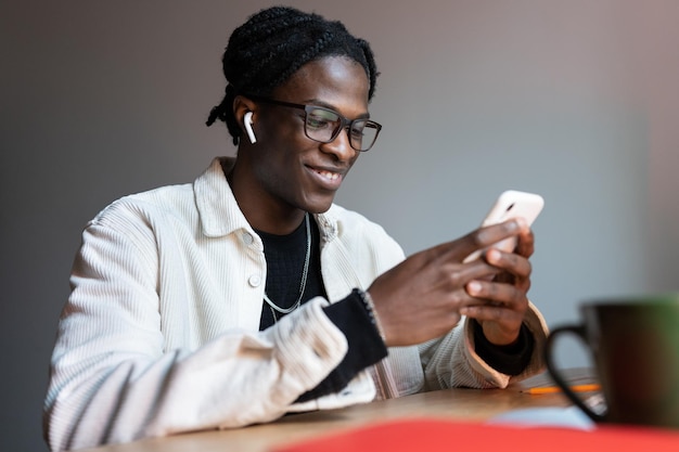 Feliz trabajador independiente negro leyendo un mensaje de texto en un teléfono inteligente mientras trabaja de forma remota desde casa