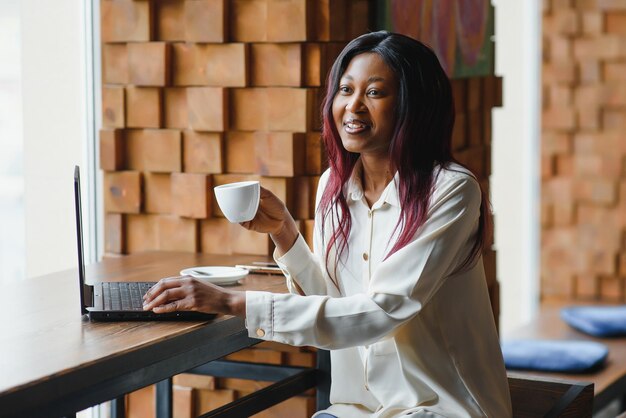 Feliz trabajadora afroamericana que usa una computadora portátil para estudiar en una computadora en una oficina de loft o una cafetería sonriente estudiante de raza mixta independiente que usa una aplicación de PC para comunicarse en línea viendo un seminario web